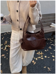 Close-up of brown leather hobo bag with silver rivets and side pocket in outdoor setting