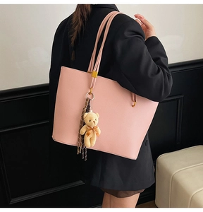Detailed close-up of a pink leather tote bag featuring a cute teddy bear charm