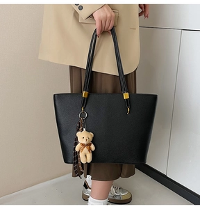 Close-up of black litchi pattern tote bag with teddy bear pendant and ribbon detail