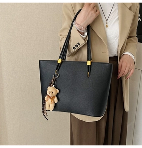 Macro detail of black pebble leather tote bag with gold ring and plush bear charm