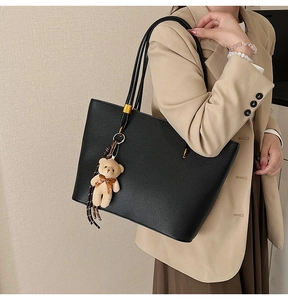 Detailed side view of black leather tote bag with gold buckle and bear charm on shoulder