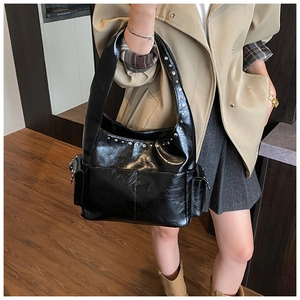 Detailed view of black patent leather shoulder bag featuring silver rivets and side pockets