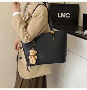 Detail of black pebbled leather tote bag with thin straps and cute bear charm accent