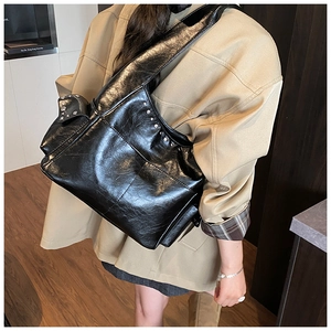 Detail of silver rivets on black leather shoulder bag with wide strap and soft texture