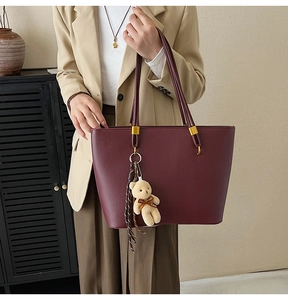 Detail of burgundy leather tote bag with plush bear charm and sturdy handles