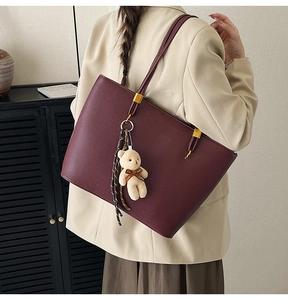 Burgundy tote bag in lychee leather texture worn by model with plush bear charm