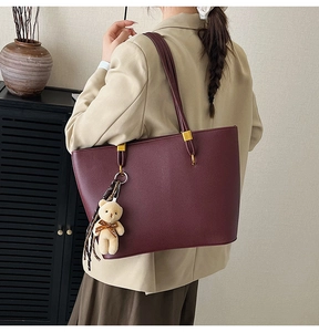 Detail of burgundy leather tote bag featuring a cute bear charm and striped strap accent