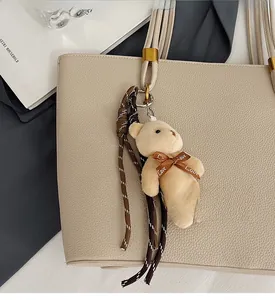 Close-up of plush bear charm with Love bow and woven rope on a textured leather tote bag