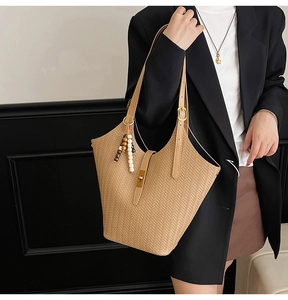 Détail d'un sac cabas tressé marron clair avec motif en V et breloque en perles