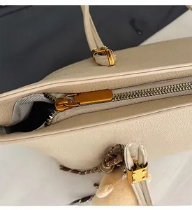Close-up of smooth metal zipper and plush bear charm on beige faux leather tote bag