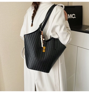 Détail du sac cabas tissé noir avec boucle dorée et breloque perlée sur trench blanc