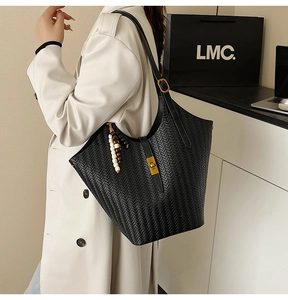 Détail d'un sac cabas tissé noir avec texture en V, boucle dorée et pendentif à perles