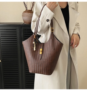 Détail d'un sac seau tissé marron café en similicuir avec pompon en perles et fermoir doré