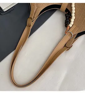 Détail de la bandoulière réglable et des perles décoratives sur un sac seau tissé kaki