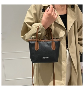 Detail of black lychee grain handbag with brown leather trim and metal Fashion logo