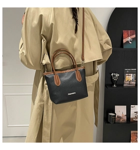 Détail du sac à main en cuir grainé noir avec anses marron porté sur l'épaule