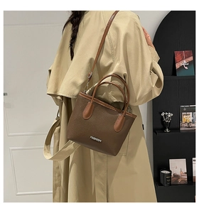 Brown lychee leather bucket bag detail with silver Fashion text on beige trench coat
