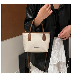 Détail du sac seau en cuir crème avec poignées brunes et logo métallique sur l'avant
