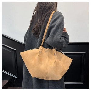 Detail view of large camel suede tote bag on grey coat showing texture and slouchy fit