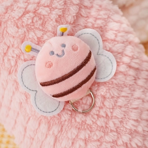 Detail of pink plush bee patch with soft faux fur texture and silver metal D-ring