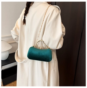 Detail of dark green velvet box bag with gold metal handle on beige trench coat
