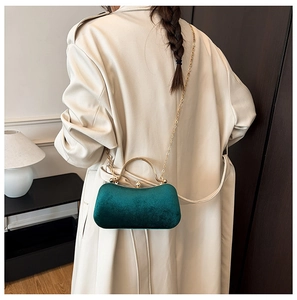 Elegant emerald green velvet box bag with gold handle shown worn as a crossbody accessory