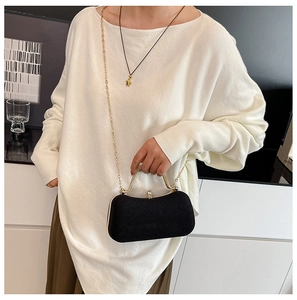 Detail of black clutch bag with gold handle and sparkling rhinestone clasp on model