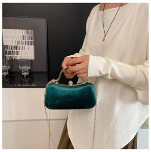 Close-up of dark green velvet evening bag with gold handle and pearl rhinestone clasp