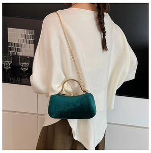 Detail of dark green velvet evening bag with gold handle and chain on a female model