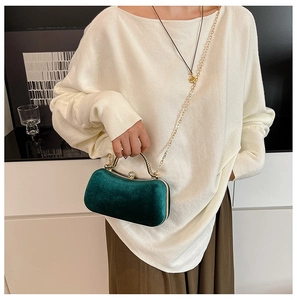 Detail of a dark green velvet evening bag with a gold metal handle and a diamond clasp