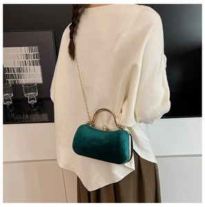 Detail of dark green velvet evening bag with gold chain and handle in a lifestyle setting