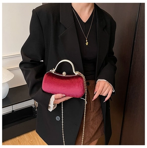 Detail of burgundy velvet clutch bag with gold handle and chain strap held by model