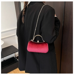 Detail of red velvet evening clutch bag with gold handle and pearl clasp on black suit