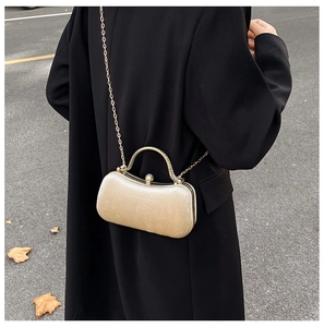 Close-up of golden evening box bag with metal handle and chain strap on a black coat