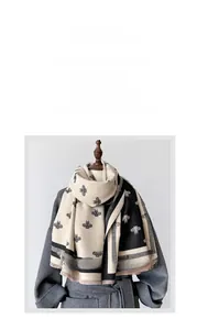 Detailed view of bee embroidery and fringe on a dual-sided beige and black cashmere scarf