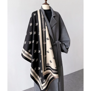 Detail of a thick double-sided cashmere scarf with bee patterns draped on a wool coat