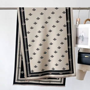 Detail of cashmere scarf featuring black bee patterns and striped borders with tassels