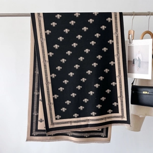 Detail of knitted scarf featuring golden bee embroidery and delicate short fringes