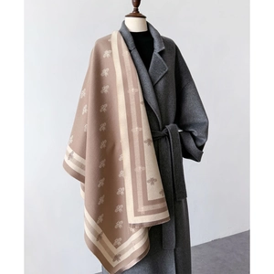 Detail of bee embroidery and fringed edges on a beige cashmere-style winter scarf