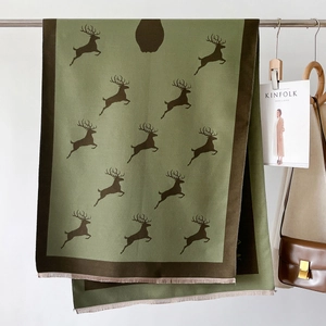 Détail d'une écharpe vert olive avec motif cerf marron et bord à franges avec accessoires