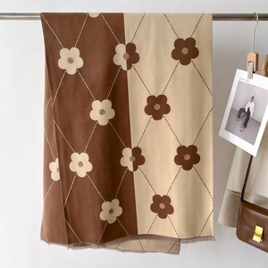 Detail of floral and argyle knit scarf with fringe displayed against a neutral background