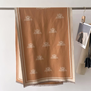 Close-up of caramel cashmere-feel scarf featuring white bee patterns and fringe detail