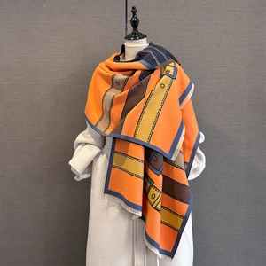 Detail of thick orange scarf featuring vintage belt buckle pattern and fringe edges