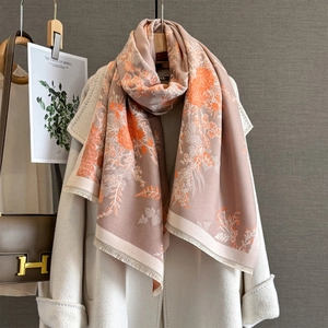 Close-up of floral cashmere scarf with orange blossoms and fine tassel edges on a coat