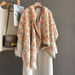 Detailed texture of beige cashmere scarf with orange floral patterns and fringed edges