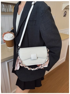 Detail of white textured shoulder bag with silver chain and striped silk scarf handle