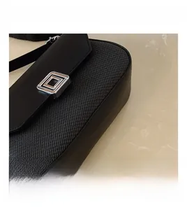 Detail shot of the woven fabric texture and metal square buckle on the black handbag