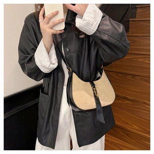 Close-up of beige crescent bag featuring black leather trim and gold metal buckle detail