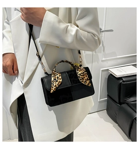 Detail of black handbag with leopard scarf handle and gold hardware on white blazer