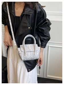 Detail of silver metallic handbag with crinkled texture worn over a black leather jacket